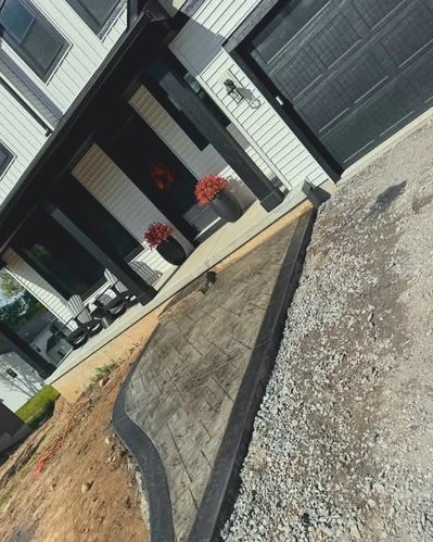 Brown stamped concrete walkway with a dark border beside gravel and a porch in Kannapolis, NC