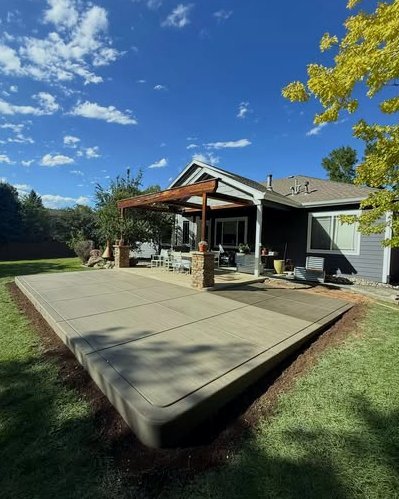 Large gray concrete patio with a rounded edge in front of a home with a wood pergola in Kannapolis, NC
